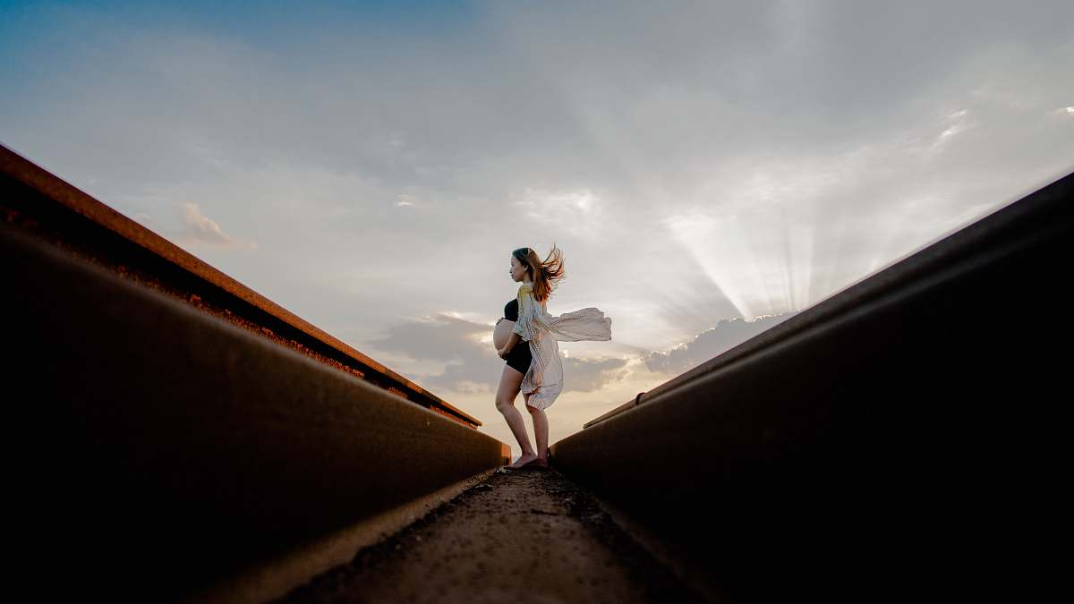 apparel pregnant woman standing near rail while holding tummy clothing