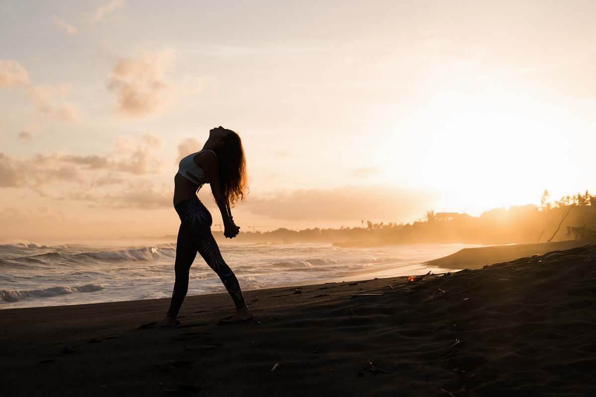 people silhouette of woman stretching her arms on seashore during sunrise person