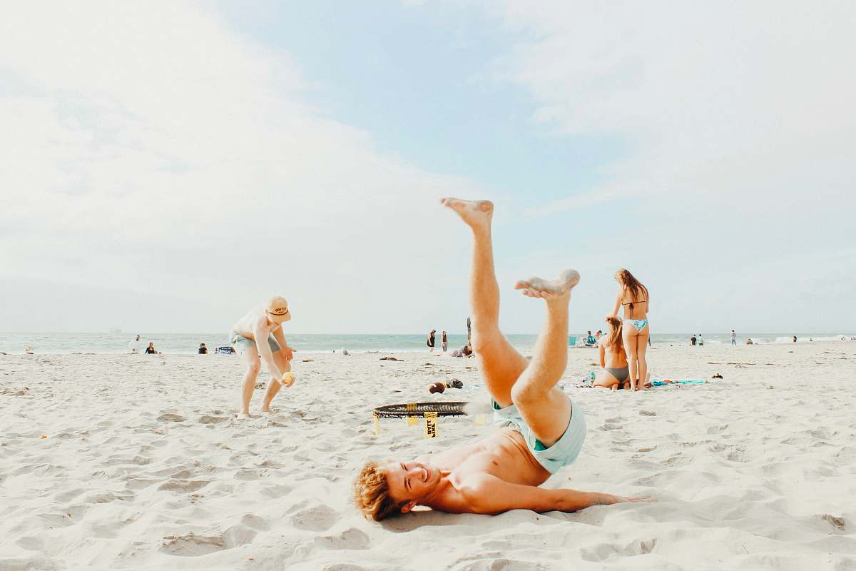 person smiling man lying on white sand during daytime apparel