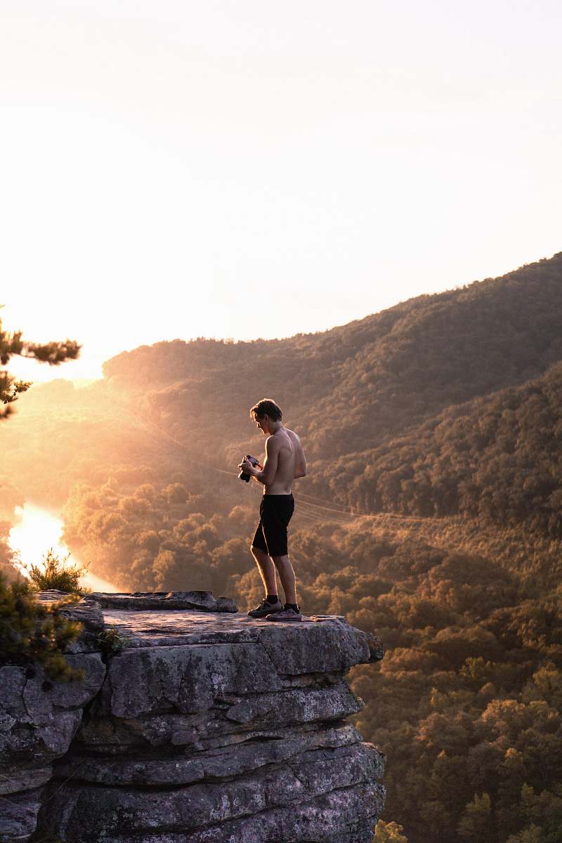 person topless man in black shorts standing near cliff at daytime people