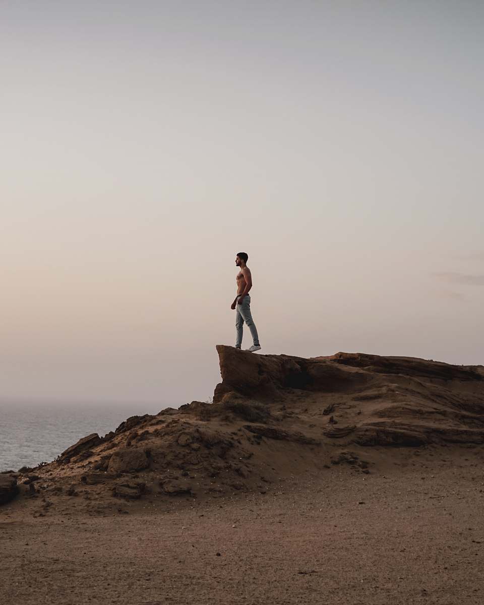 person topless man standing on rocky hill standing
