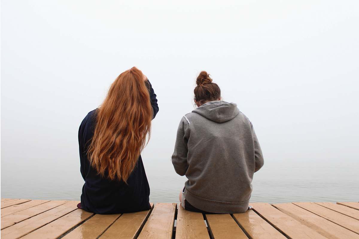 person two women sitting on wooden dock over body of water people