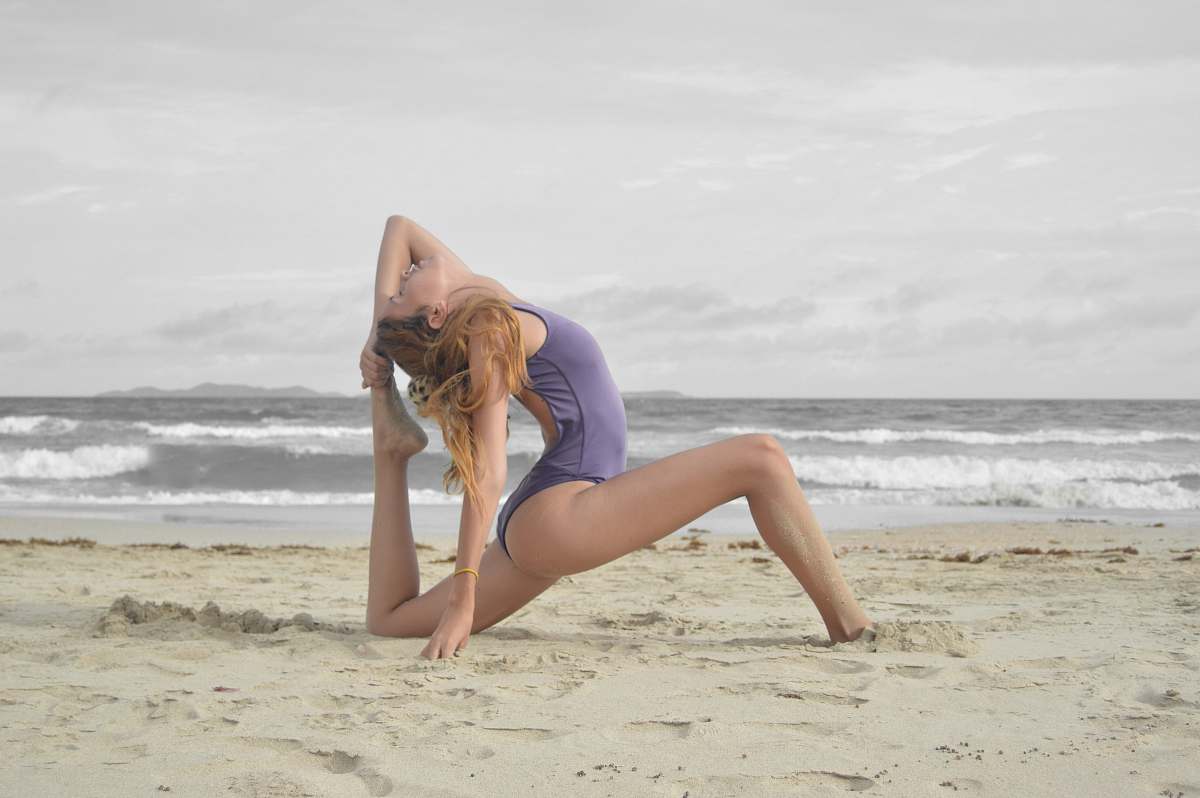 person woman doing ballet stunt on beach shore stretch