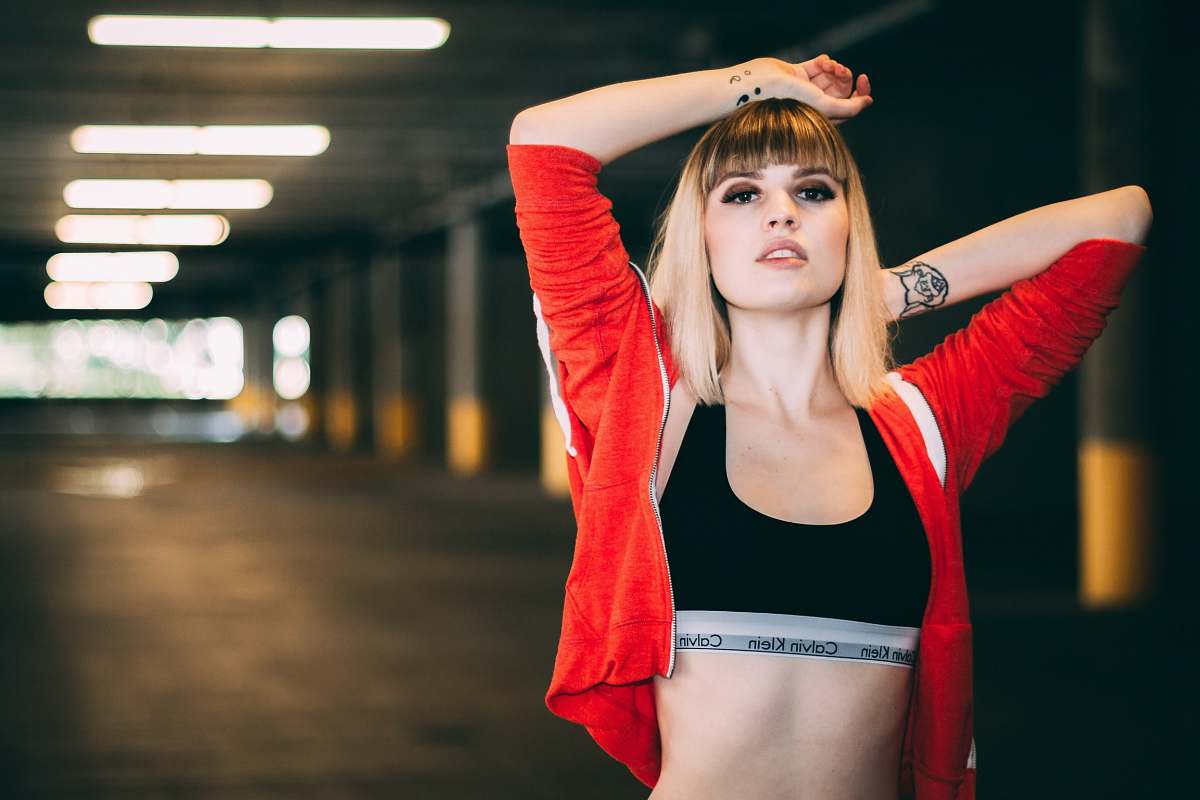 person woman in black sports bra and red jacket posing in parking lot people