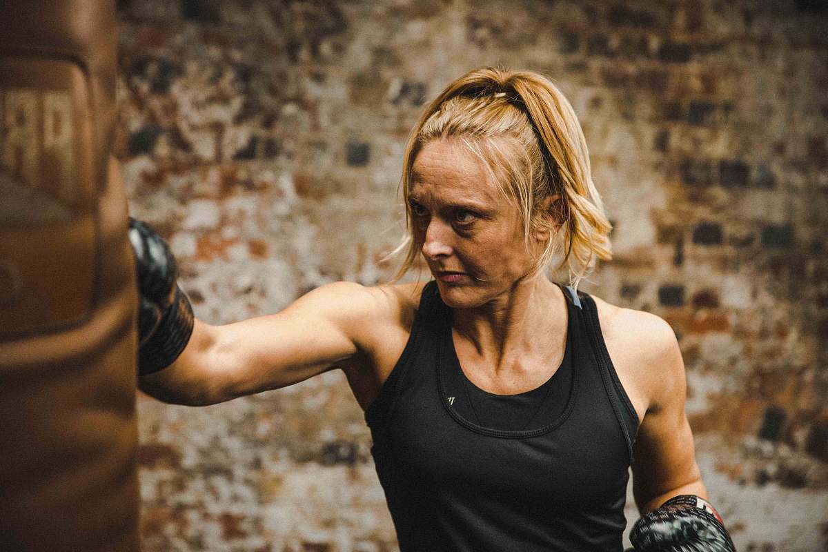person woman in black tank top punching brown heavy bag finger