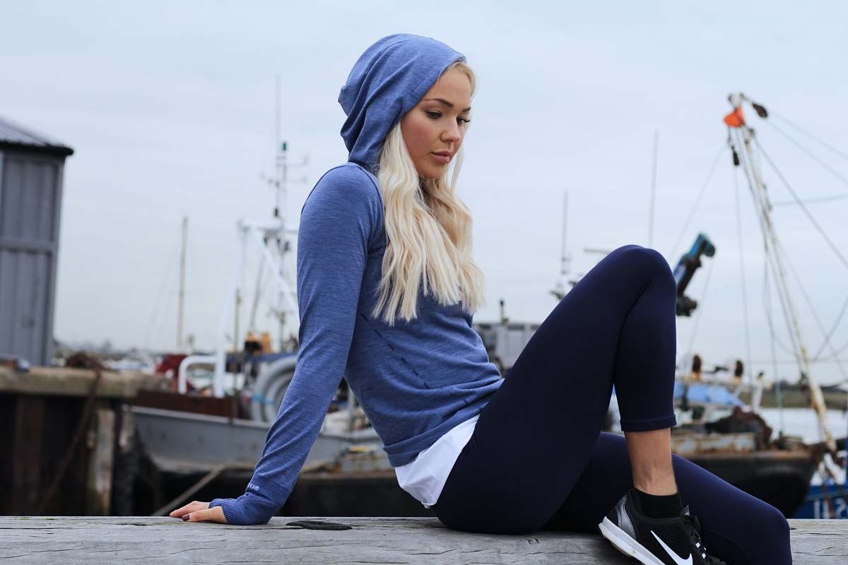 person woman in blue hoodie and black leggings lounging at gray concrete surface working out