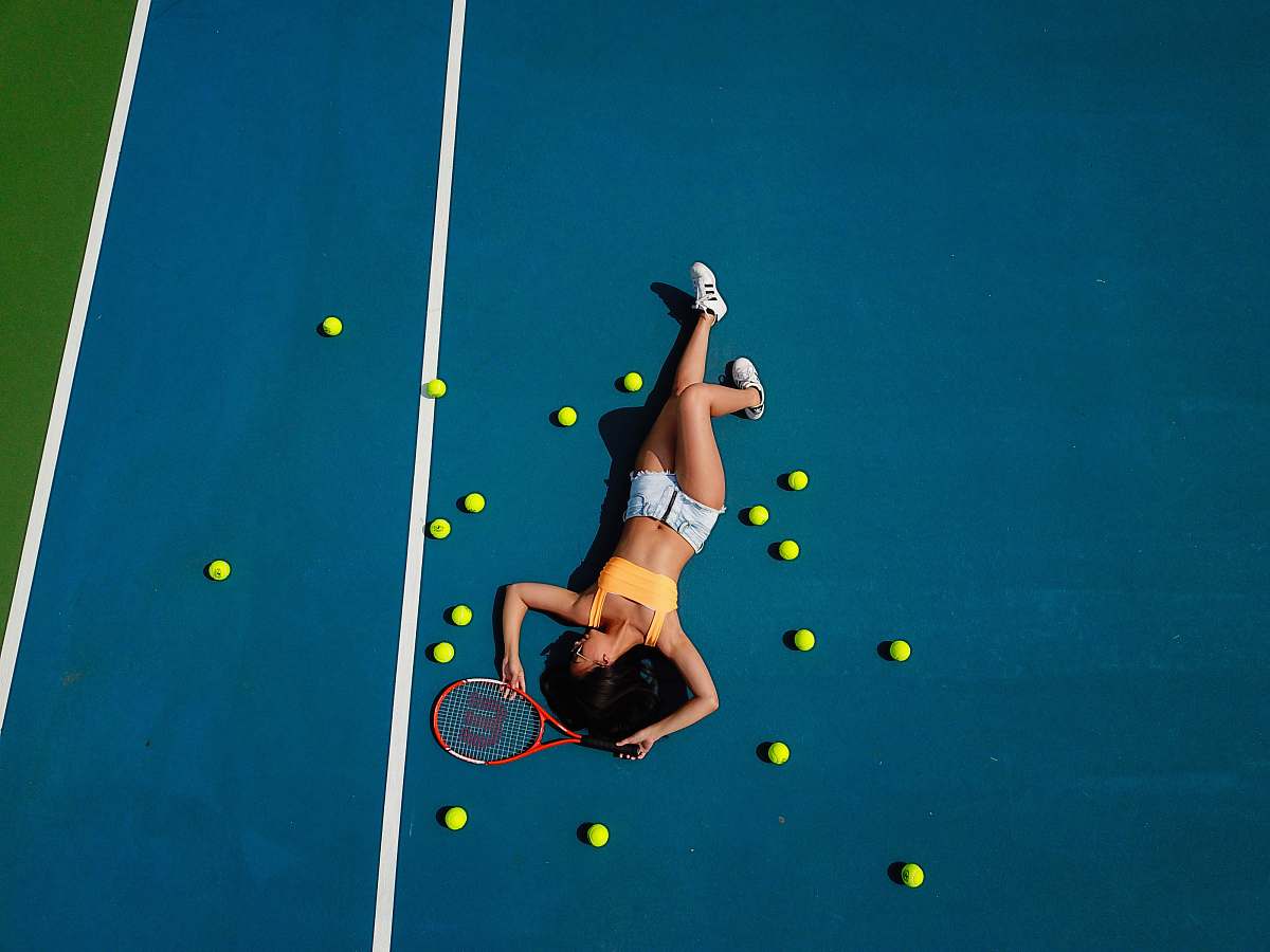 person woman in yellow crop top laying down on hard court sport