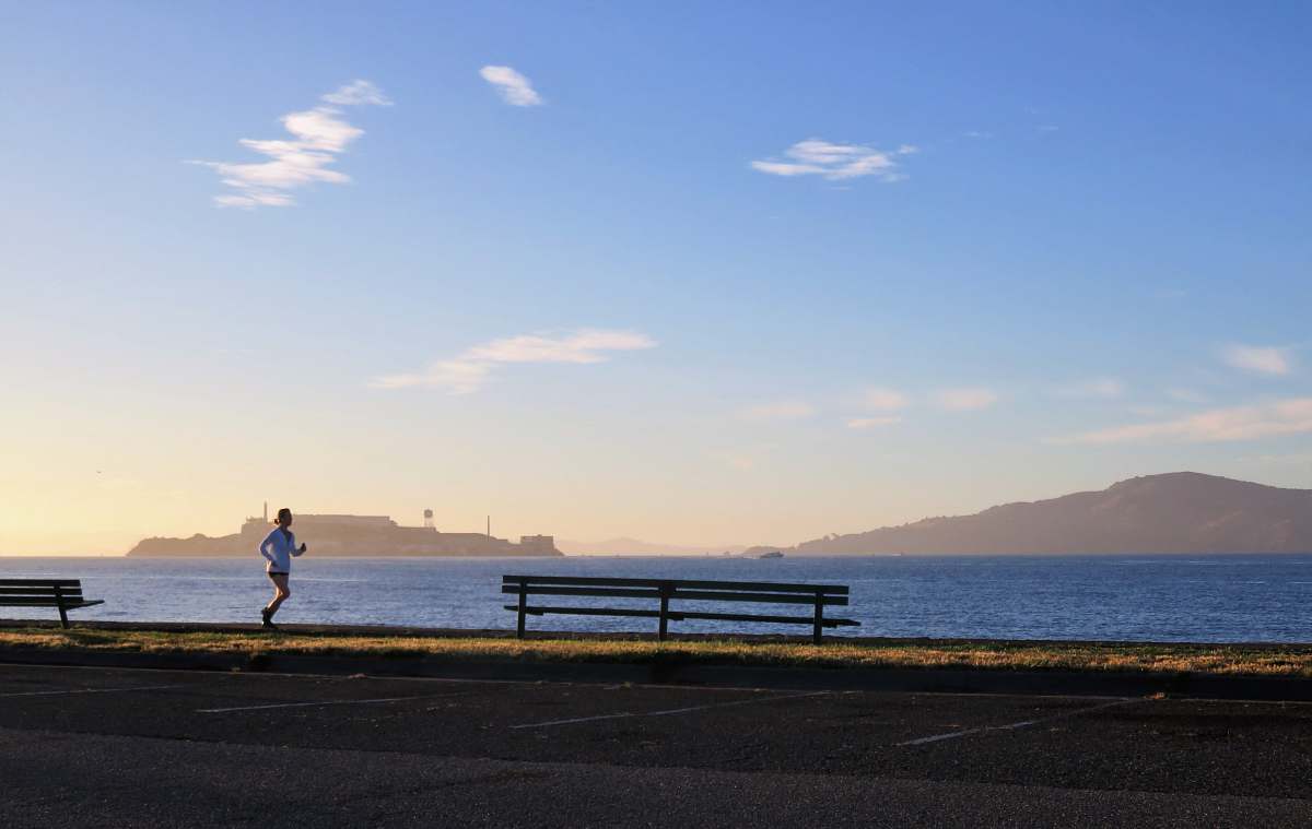 person woman jogging near ocean bench