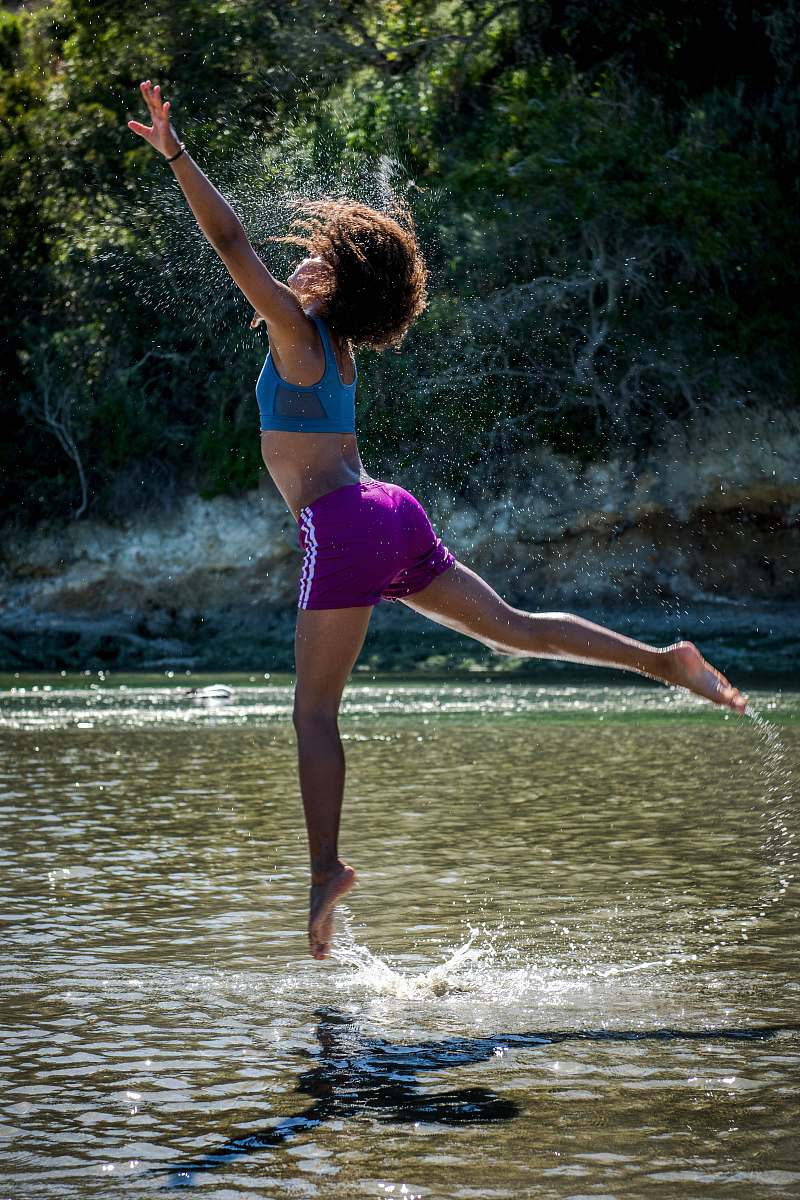person woman jumping on body of water near trees during daytime people