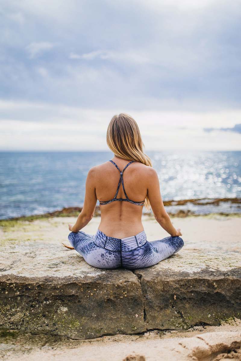 person woman meditating front of sea at daytime back