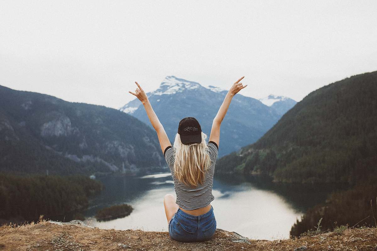 person woman sitting on cliff raising both hands people