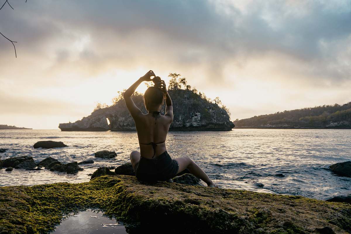 sport woman sitting on rock formation facing the beach person