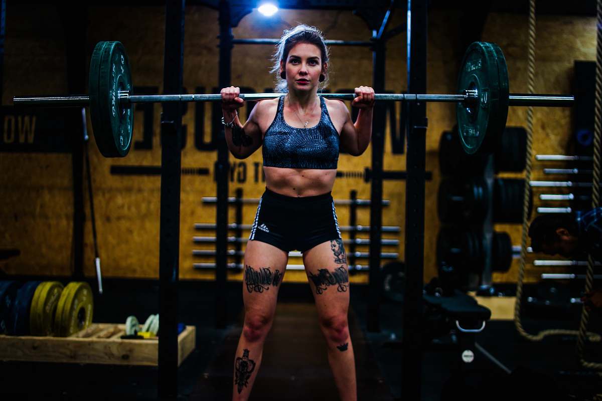 person woman standing and carrying barbell gym