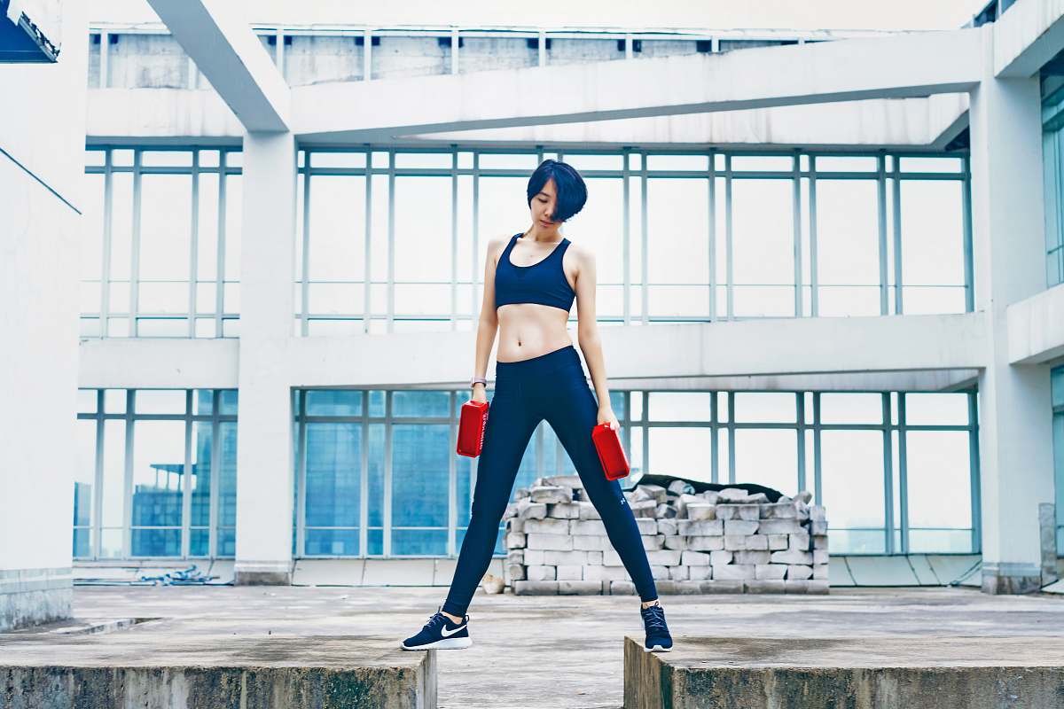 person woman wearing black sports bra and pants while holding two red weights people