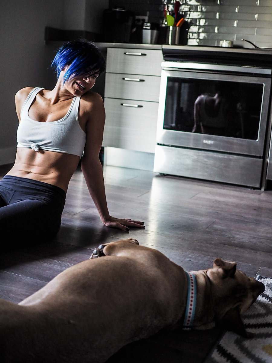 person woman wearing grey sports bra sitting on wooden floor with short-coated dog people
