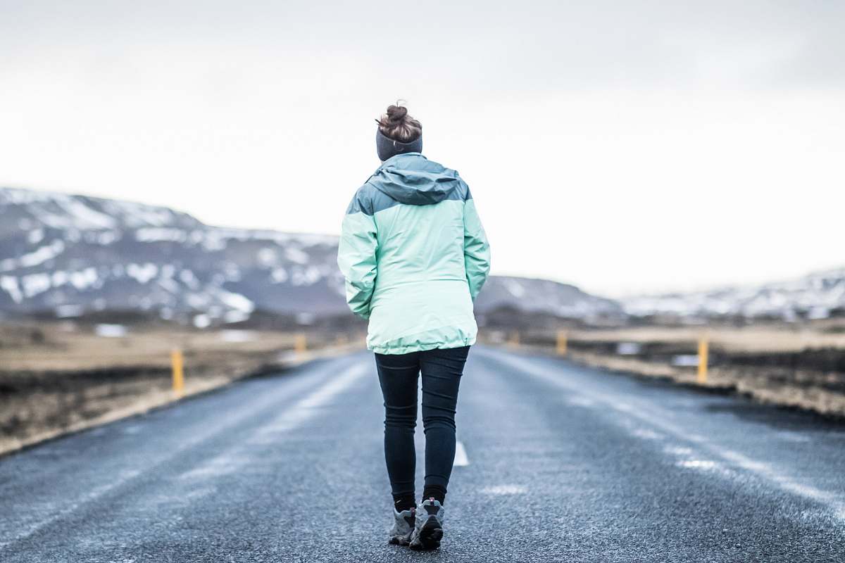 people woman wearing teal jacket and black pants walking on concrete road person