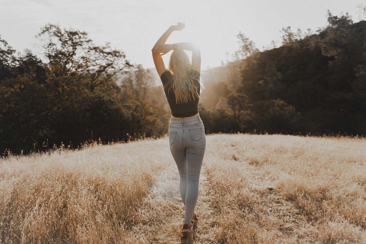 person women's black crew-neck shirt and gray jeans walking on brown grass pathway field sport
