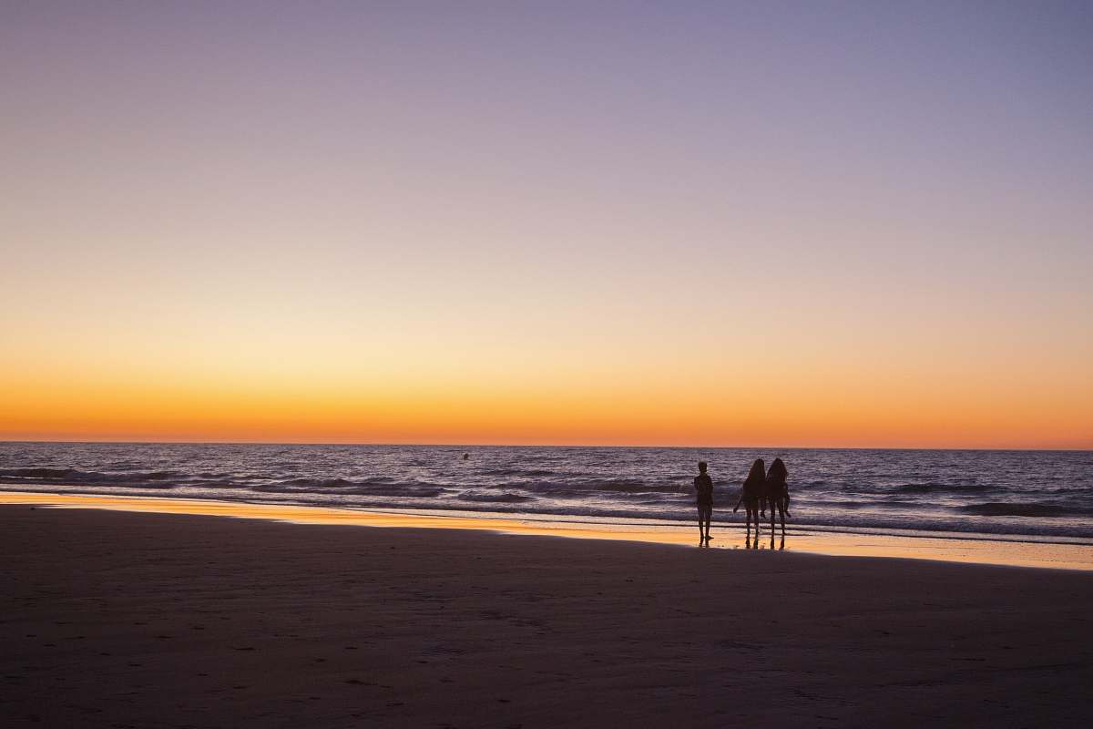 sea 3 peopls standing on shore under the sunset ocean
