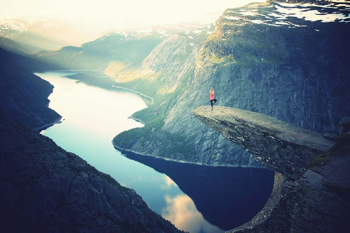 mountain person standing on rock ledge doing yoga pose yoga