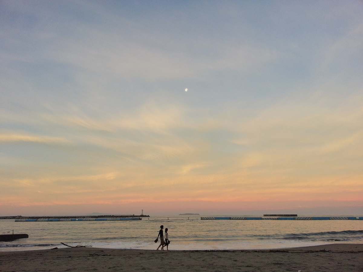 ocean two people walking near seashore under blue and orange sky outdoors