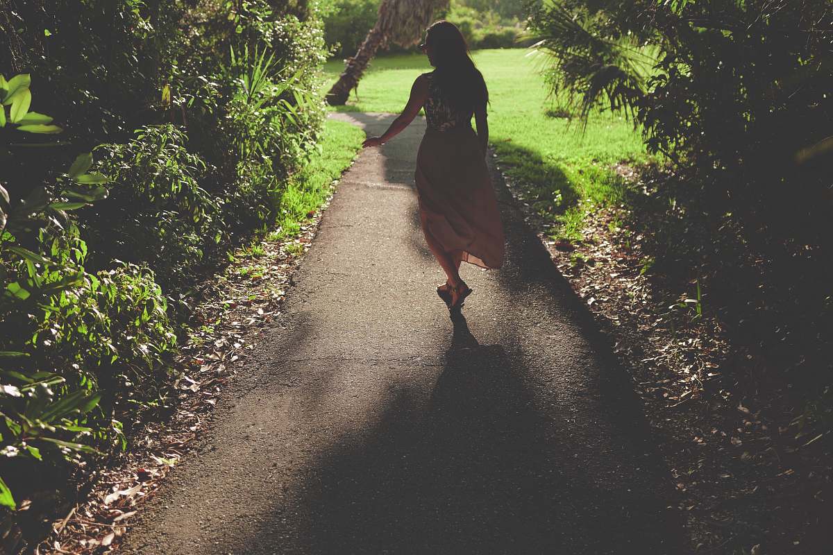 road woman in pink dress standing on gray concrete pavement near green plants plant