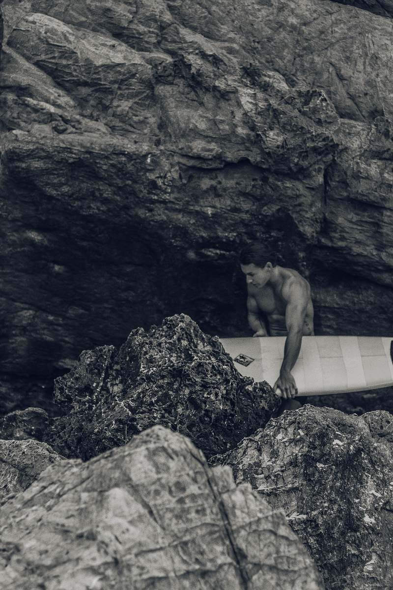 nature man holding surfboard beside rock rock