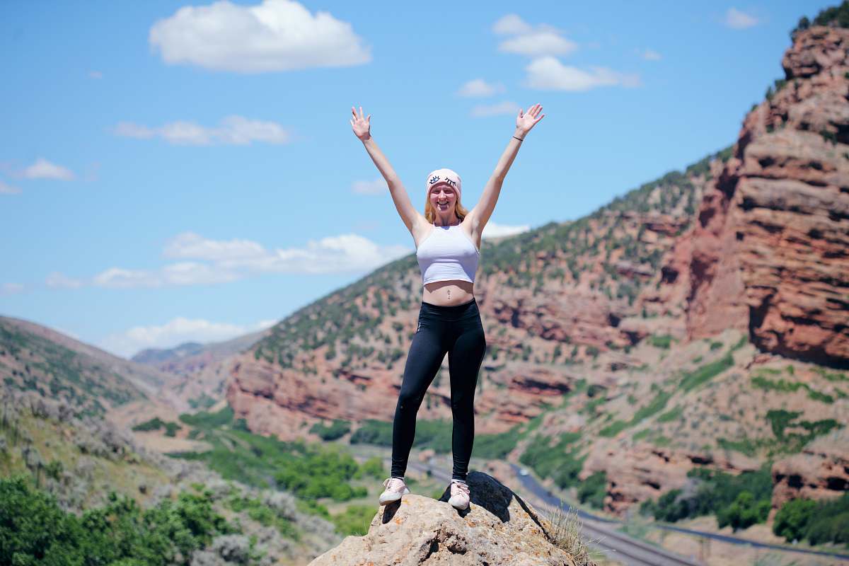human woman wearing white top and black pants standing on cliff person