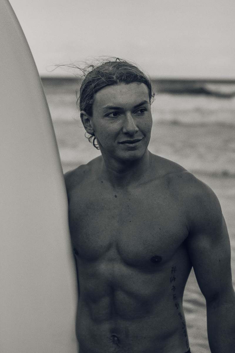 human grayscale photo of man holding surfboard skin