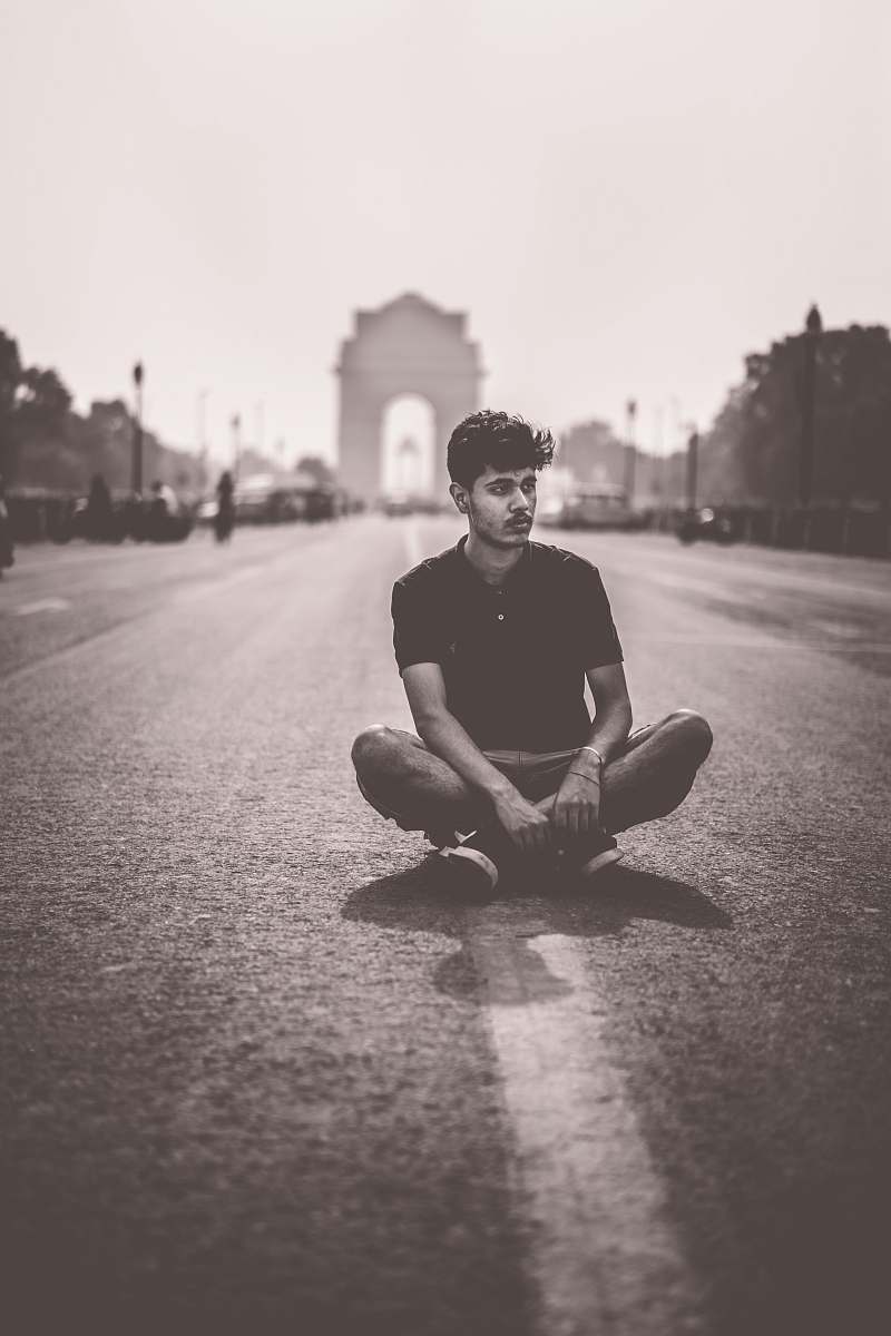 human grayscale photo of man sitting on road sitting