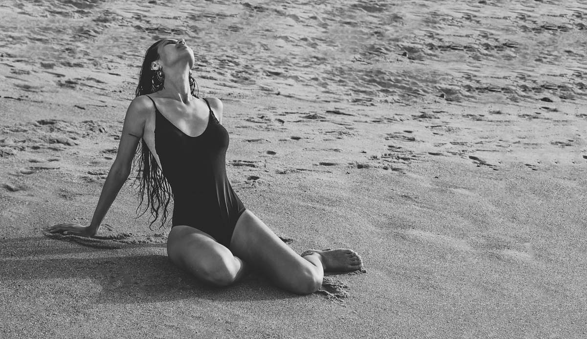 human grayscale photo of woman sitting and bending her body on seashore black-and-white