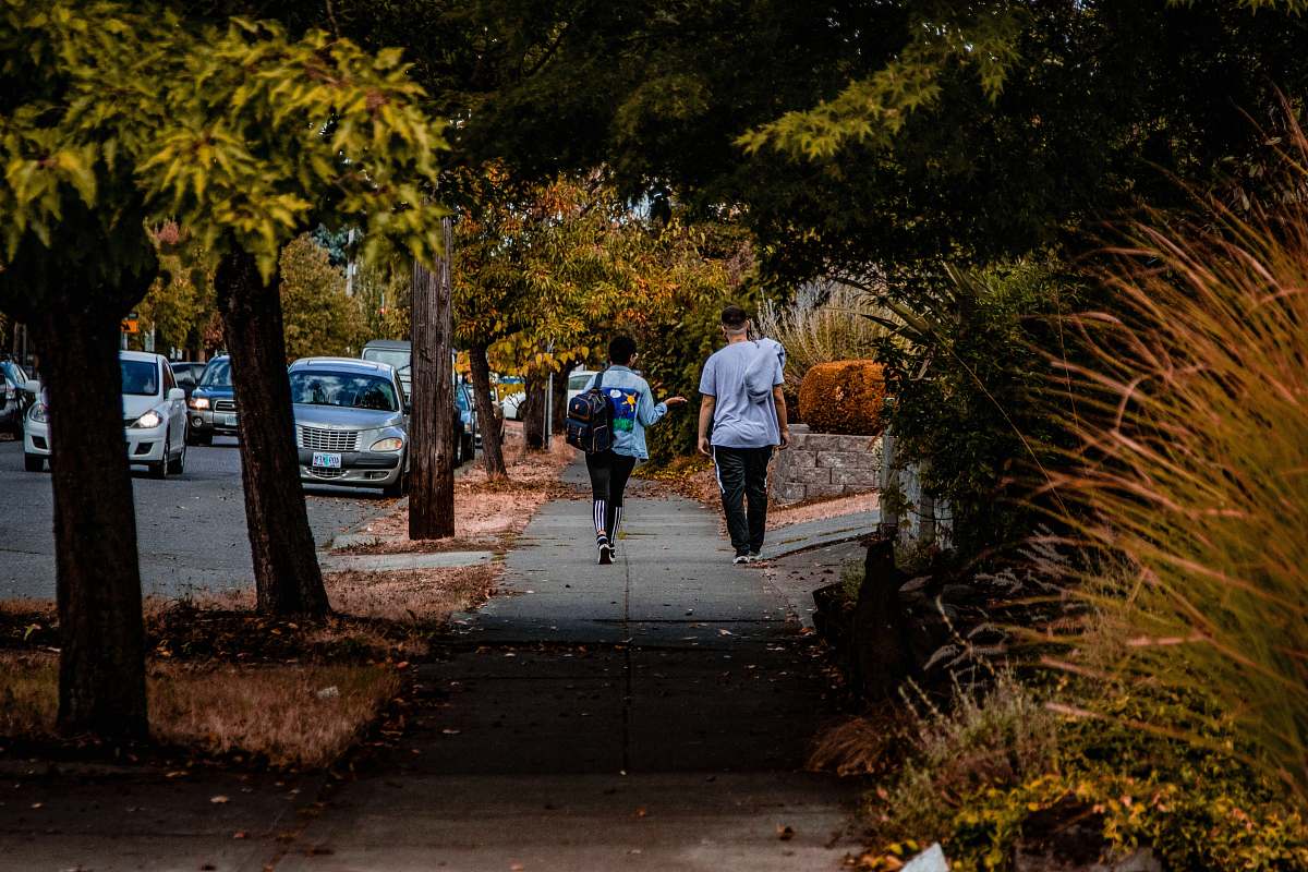 human man and woman walking on sidewalk near road and cars path