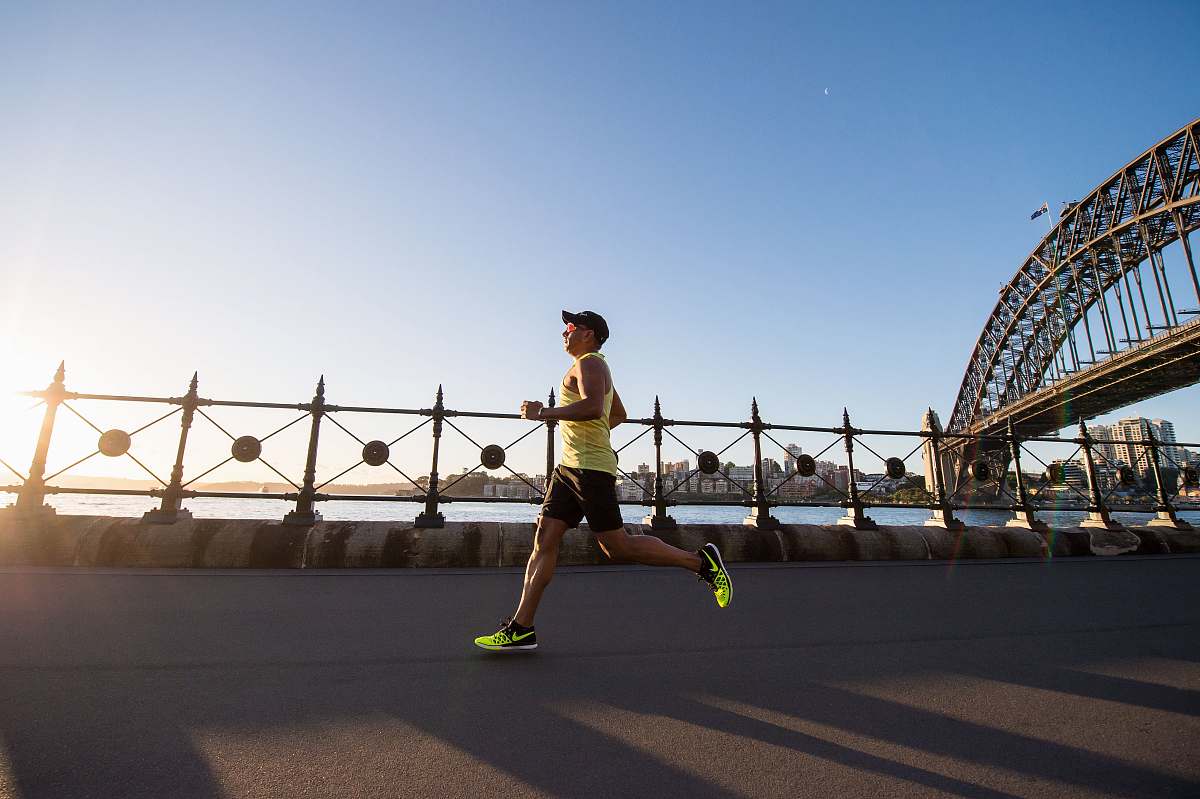 human man in yellow tank top running near shore working out