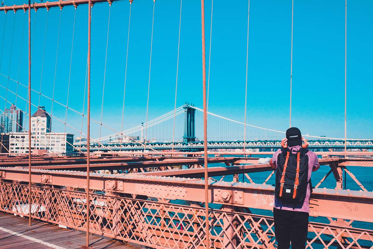 human man standing on Brooklyn bridge facing Manhattan bridge during daytime people