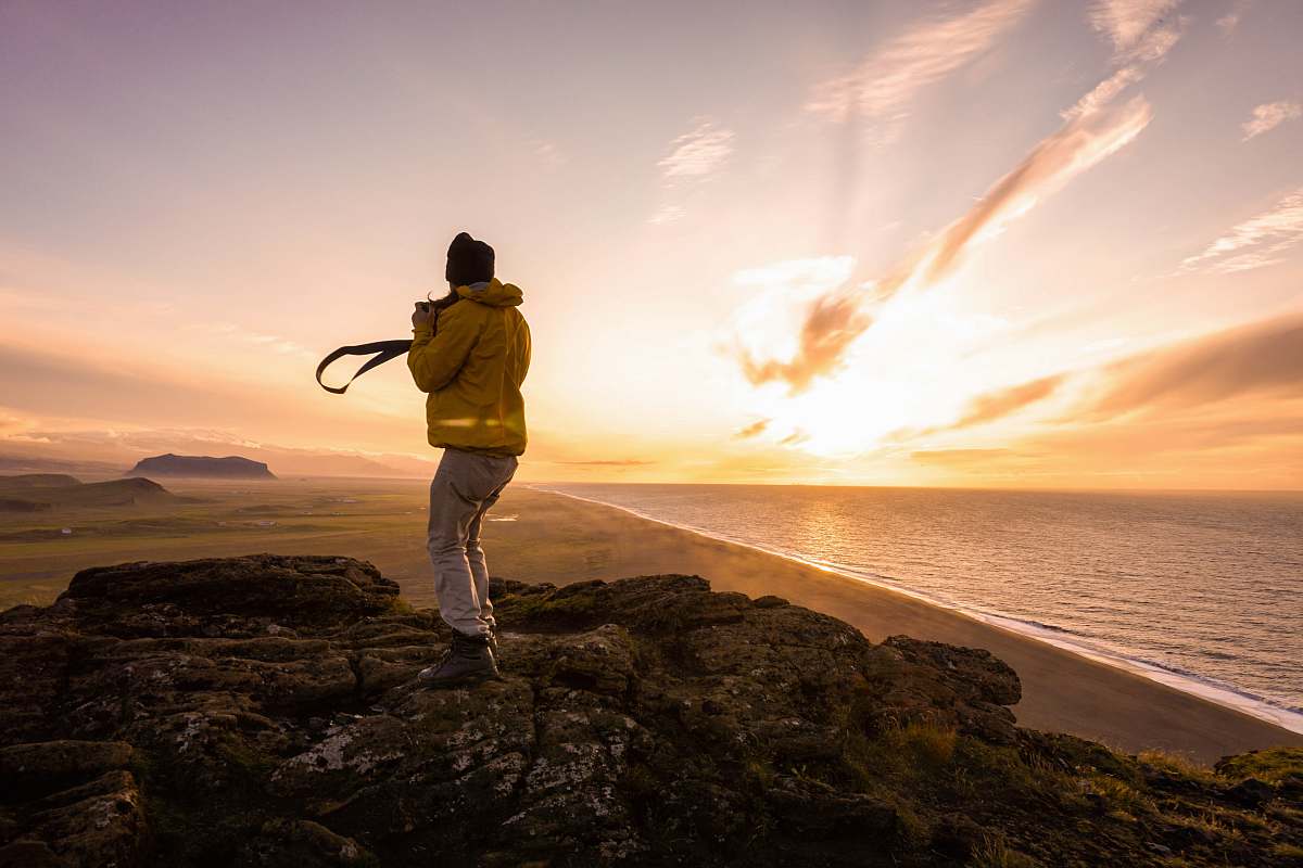 A serene scene unfolds as a human man stands on a rugged rocky beach, his camera poised to capture the breathtaking hues of a sunset. The vibrant oranges, pinks, and purples of the sky create a stunning backdrop, ideal for use in travel blogs, lifestyle articles, and social media content. This image embodies the tranquility and beauty of nature, making it a perfect choice for anyone looking to evoke a sense of adventure and appreciation for the outdoors.