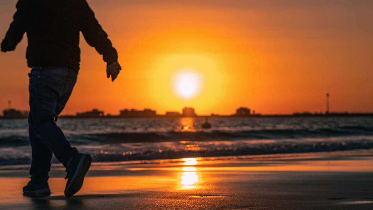 human man walking on seashore during sunset apparel