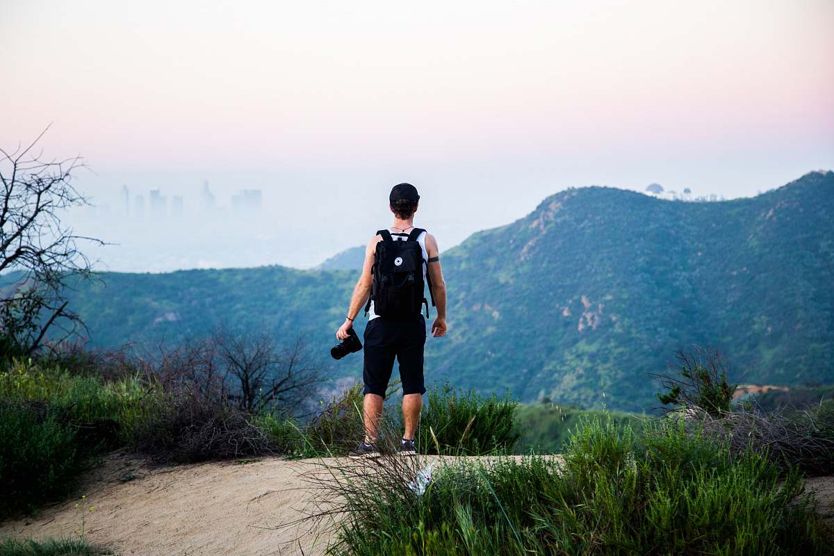 human man wearing black backpack standing near mountain at daytime people