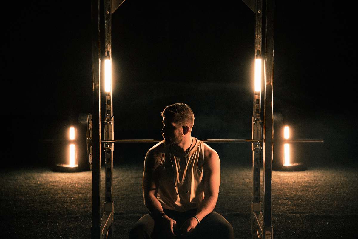 human man wearing grey tank top sitting on brown wooden bench clothing