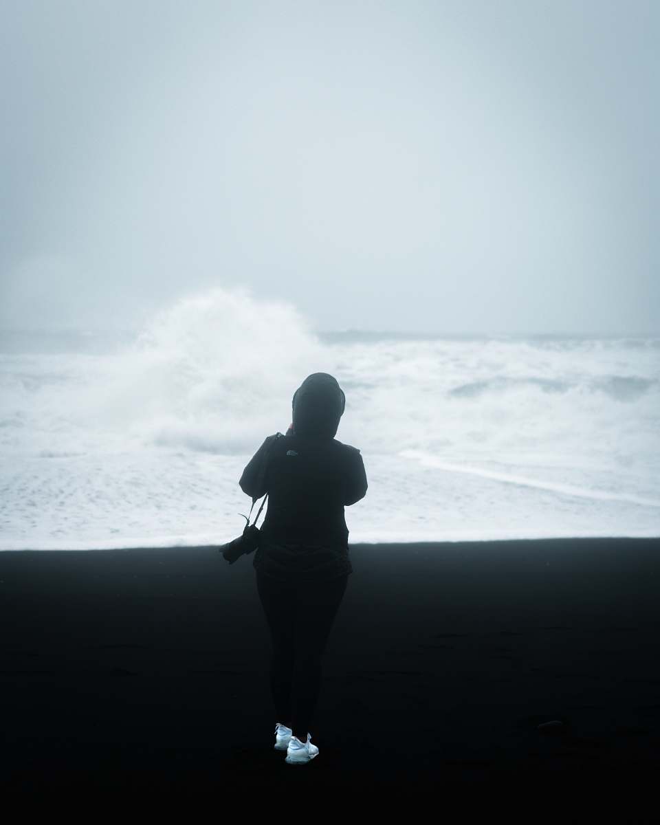 human man wearing jacket with camera standing in front of ocean waves nature