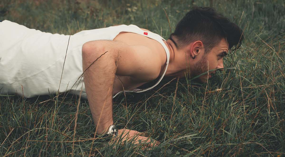 human man wearing white tank top pruning on green grass grass
