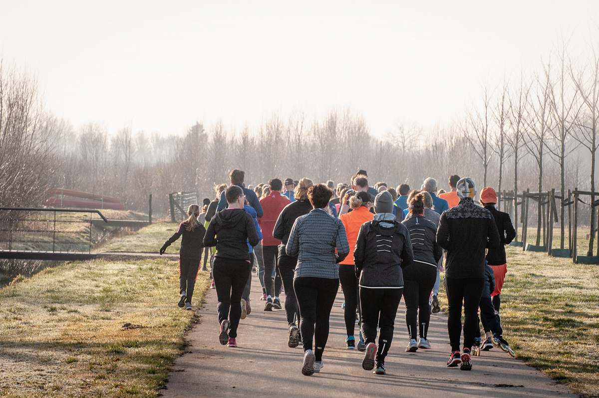 human people running on concrete road beside leafless trees during daytime footwear