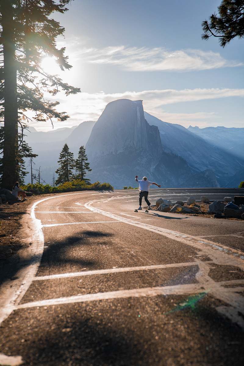 human person skating on road viewing mountain under blue and white skies asphalt