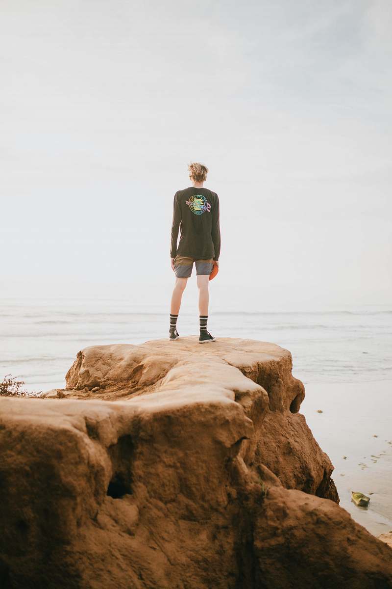 human person standing at the edge of a cliff in front of ocean during daytime people