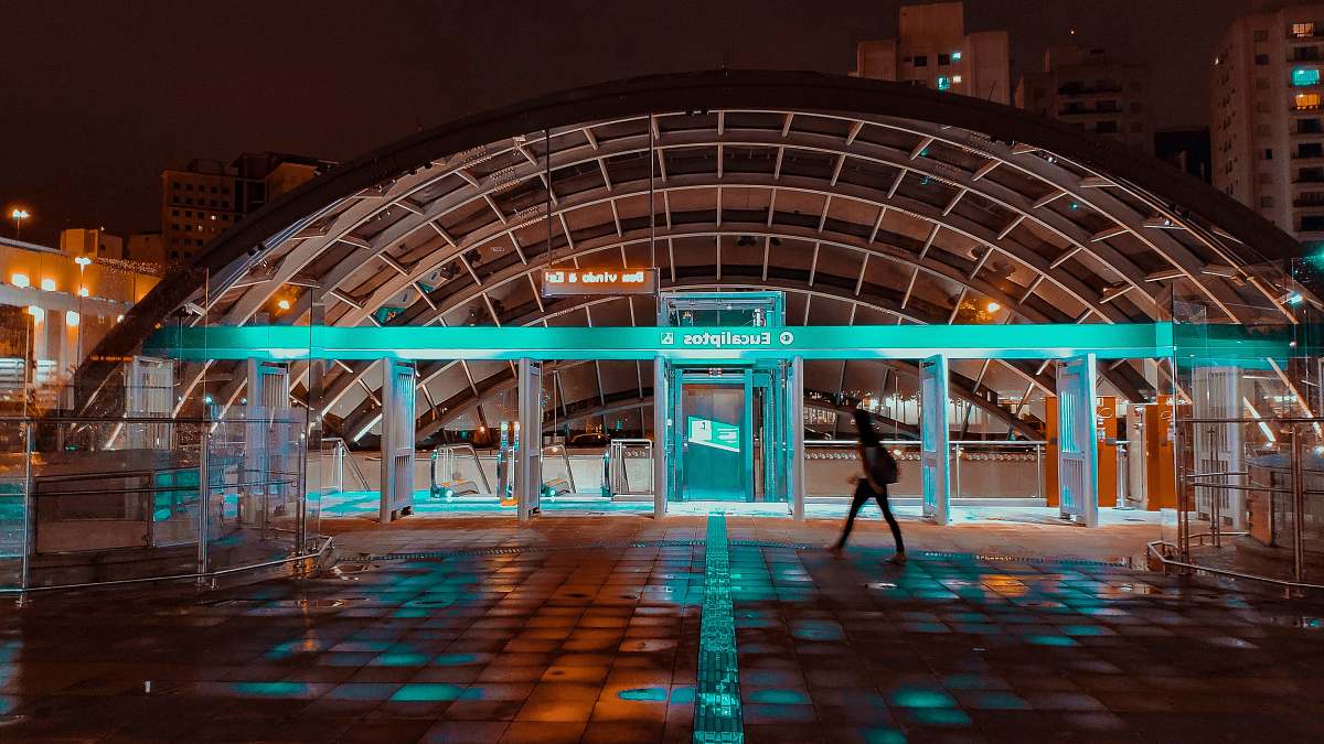 Human Person Walking Beside Waiting Shed With Teal Light At Night Time 