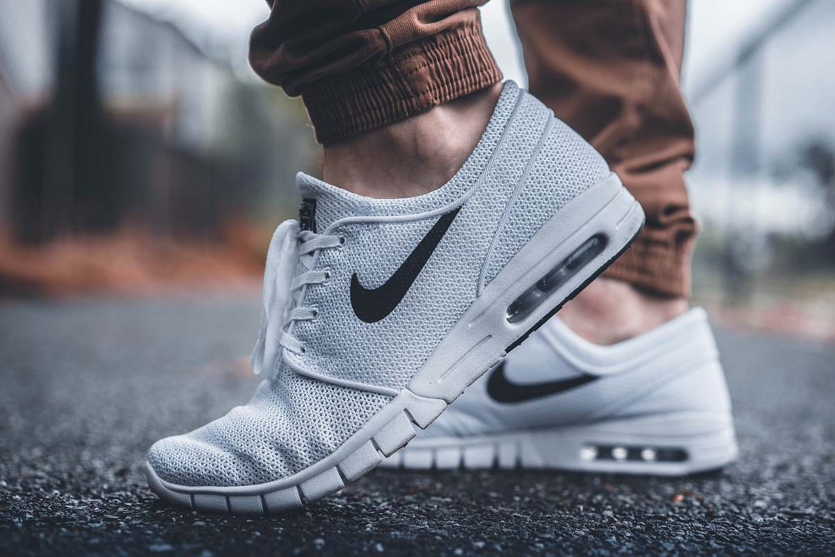 nike person wearing white Nike running shoes standing on black concrete path shoes