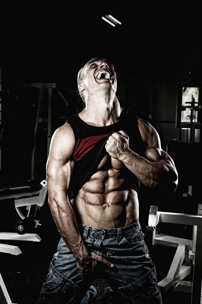 human smiling man holding up his black tank top and and blue denim bottoms while looking up fitness