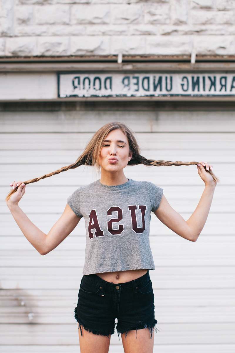 people standing woman holding her pig tail tied hair pouting her lips in front of building woman