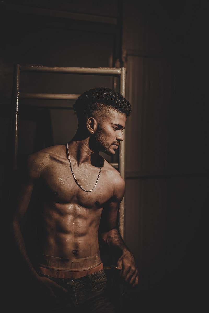 human topless man wearing necklace while leaning against rack people