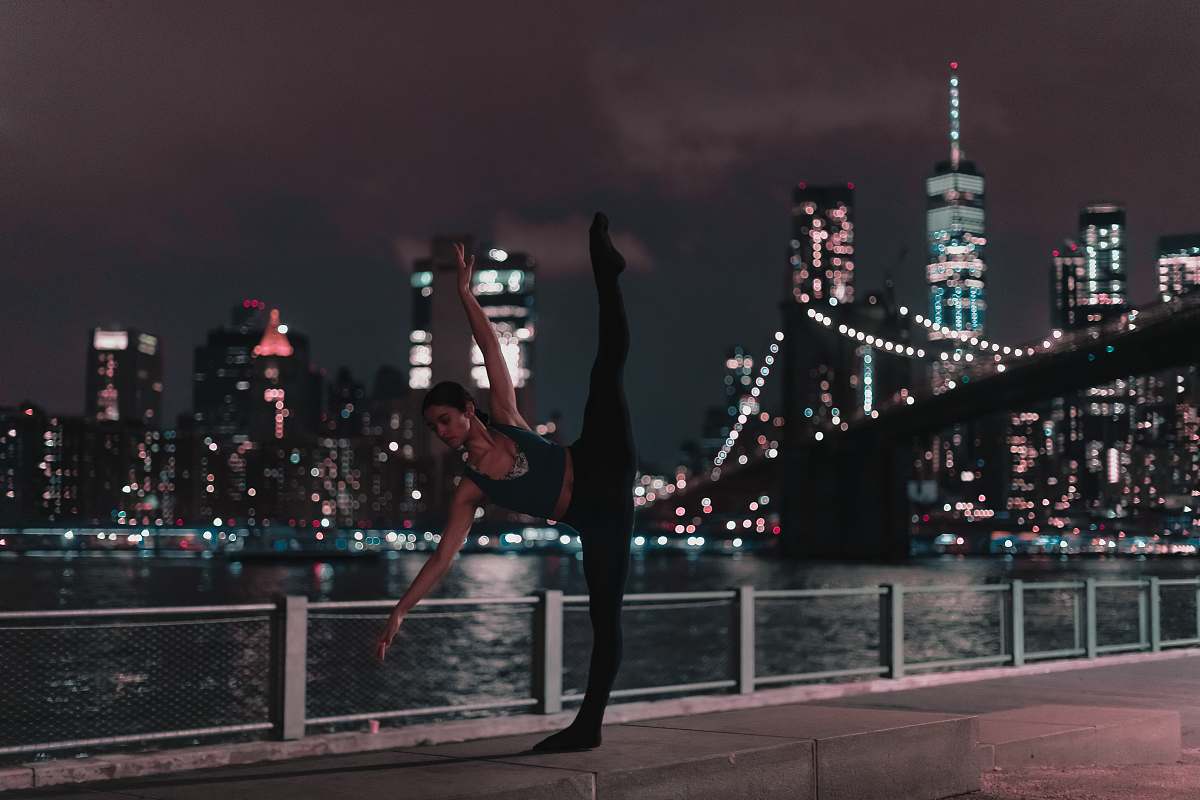 human woman in black sports bra and tights doing ballet position on sidewalk during nighttime dance