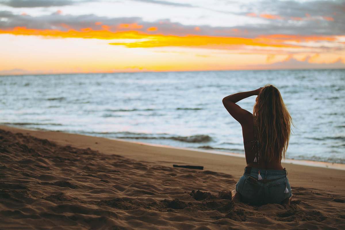 human woman sitting on seashore looking at sea during golden hour ocean