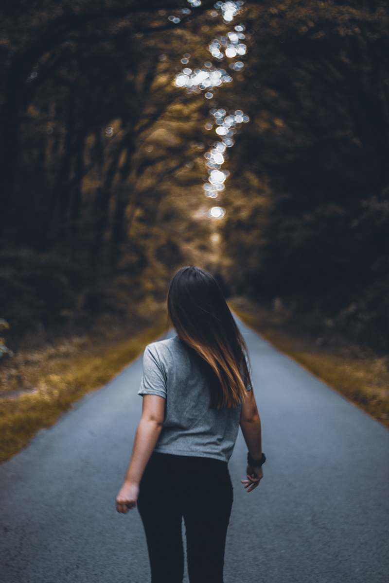 human woman walking on empty road between trees apparel